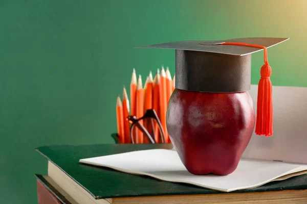 Graduate cap and apple on old book at library green wall backgro — Stock Photo, Image