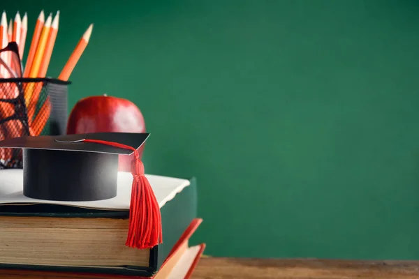 Graduate cap and apple on old book at library green wall backgro — Stock Photo, Image