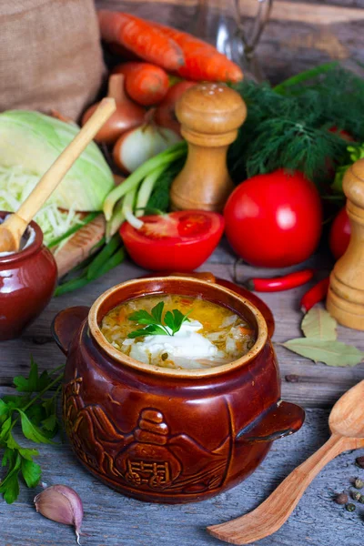Cabbage soup in a clay pot on a background of ingredients for cooking soup, selective focus