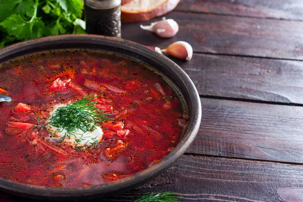 National traditional Ukrainian soup made from beets and vegetables - borscht with sour cream and fresh herbs in a clay bowl, horizontal, copy space — Stock Photo, Image