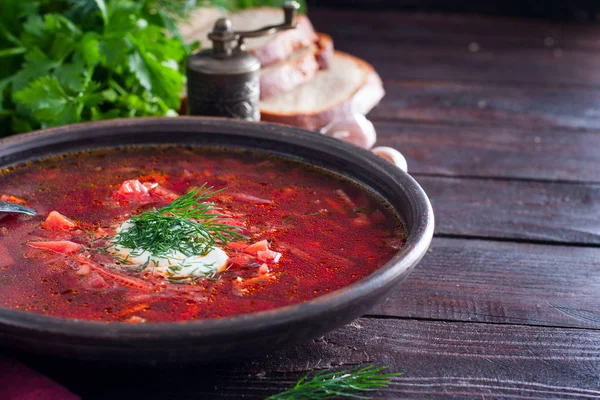 National traditional Ukrainian soup made from beets and vegetables - borscht with sour cream and fresh herbs in a clay bowl, horizontal, copy space — Stock Photo, Image