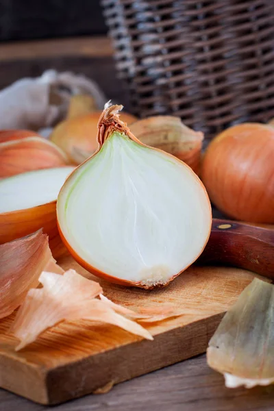 Grote uienoogst in een rieten mand. Bolvormige ui is rijk aan vitaminen, nuttige lente. Ui schil op een houten ondergrond. Grote uien zijn van bovenaf te zien. — Stockfoto