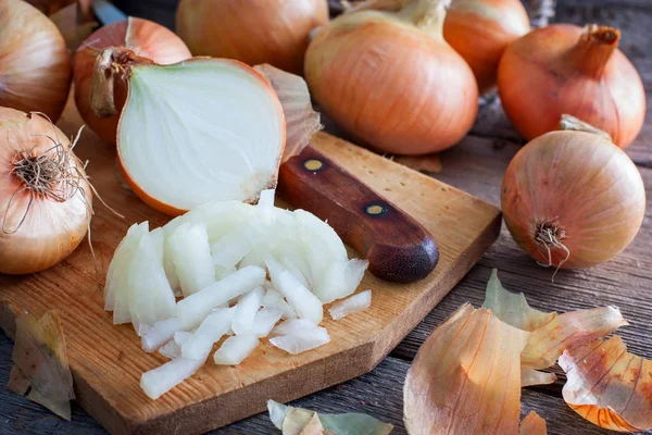 Fijngehakte uien naast hele bollen en bolsters op een houten tafel, horizontale — Stockfoto