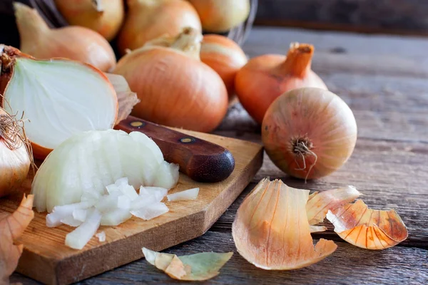 Fijngehakte uien naast hele bollen en bolsters op een houten tafel, horizontale — Stockfoto