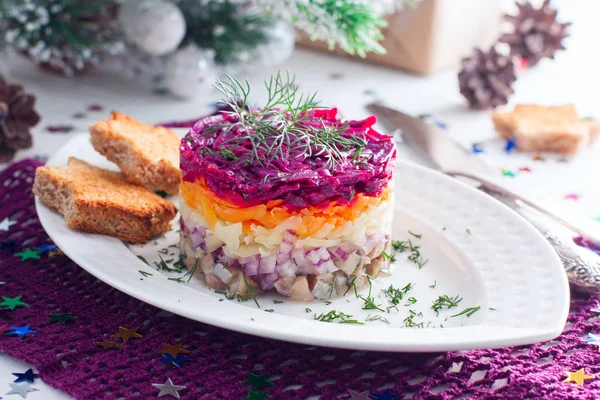 Новогодний салат "Селедка под шубой" на белой тарелке в рождественских украшениях, горизонтальный — стоковое фото