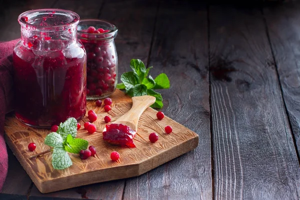 Cowberry jam in a glass jar on a wooden board with fresh berries, horizontal, copy space