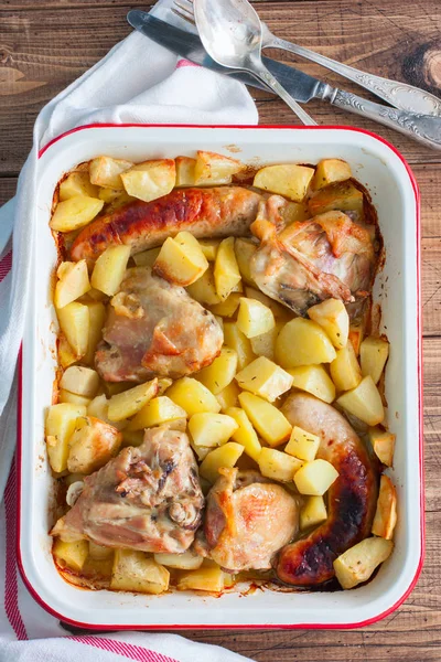 Baked potatoes with sausages and chicken in enameled form, top view — Stock Photo, Image