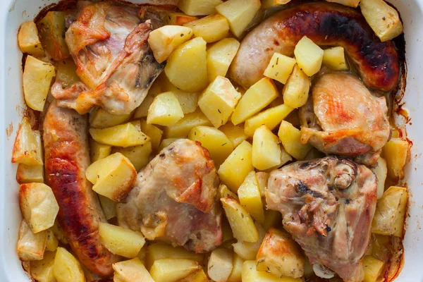 Baked potatoes with sausages and chicken in enameled form on a wooden table, top view, horizontal — Stock Photo, Image