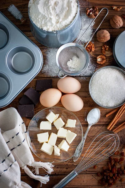 Ingredientes para cozinhar cupcakes: manteiga, ovos, farinha, açúcar, nozes, passas, forma em uma mesa de madeira, vista superior, foco seletivo — Fotografia de Stock