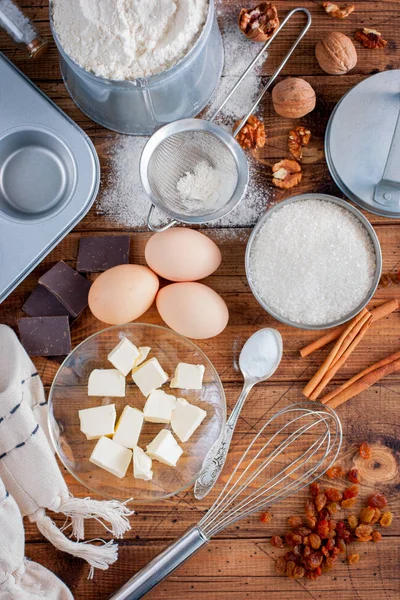 Ingredientes para cozinhar cupcakes: manteiga, ovos, farinha, açúcar, nozes, passas, forma em uma mesa de madeira, vista superior, foco seletivo — Fotografia de Stock