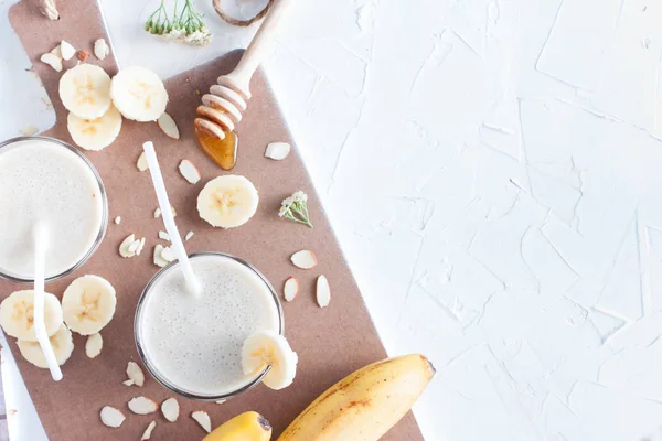 Smoothie à la banane avec banane, lait, amandes et miel dans des verres en verre sur une table blanche, vue du dessus, horizontal, mise au point sélective — Photo