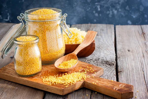 Raw organic natural millet in glass jars, spoon on a wooden table, horizontal, copy space — Stock Photo, Image