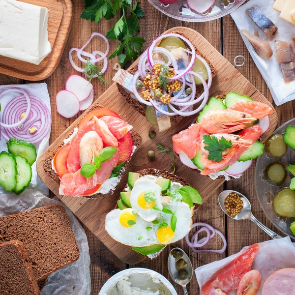 Варианты традиционных датских открытых бутербродов на ржаном хлебе на завтрак на деревянном столе, вид сверху, площадь — стоковое фото