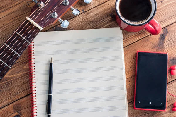 Guitar, black coffee, smartphone and clean note book on a wooden table, top view, horizontal, copy space, music concept