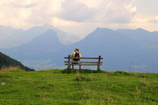 Sankt-Wolfgang, Avusturya'ya seyahat edin. Genç adam dağların manzarası yla bir bankta oturuyor.. — Stok fotoğraf