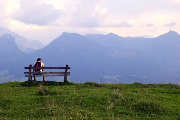 Podróż do Sankt-Wolfgang, Austria. Młody mężczyzna siedzi na ławce z widokiem na góry. — Zdjęcie stockowe