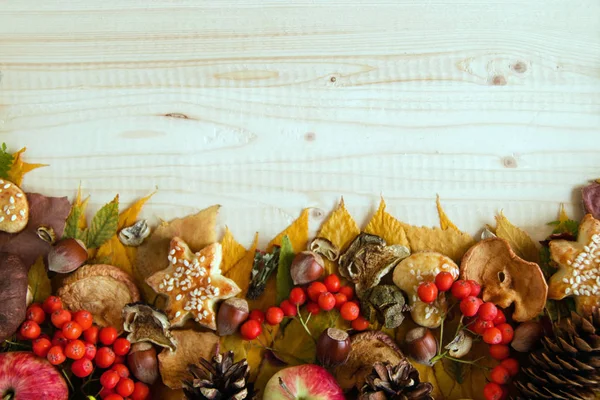 カラフルな秋から枠を離れると、キノコ、ローズヒップ、rowanberry、リンゴ、ナッツ、コーン、木製の背景にクッキー. — ストック写真