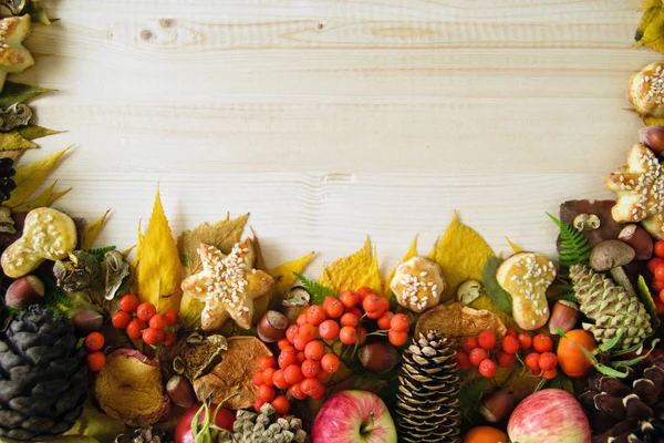 Frontiera da colorate foglie autunnali, funghi, rosa canina, rowanberry, mele, noci, coni e biscotti sullo sfondo di legno . — Foto Stock