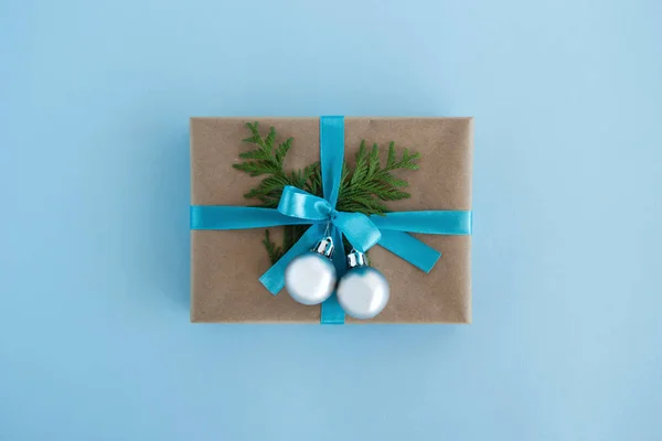 Caixa de presente embrulhado de papel artesanal, fita azul e ramos de abeto decorados e bolas de Natal de prata no fundo azul, vista superior. Presente de Natal . — Fotografia de Stock