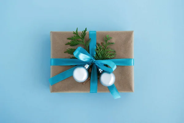 Luxe-geschenketui van Kraft papier, blauw lint gewikkeld en ingericht fir takken en zilveren kerstballen op de blauwe achtergrond, bovenaanzicht. Kerstcadeau. — Stockfoto