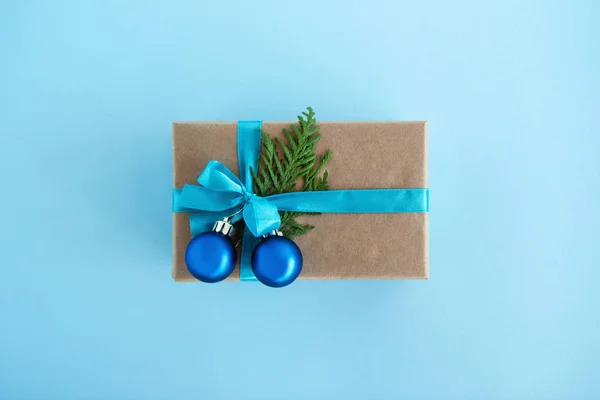 Luxe-geschenketui van Kraft papier, blauw lint gewikkeld en ingericht fir takken en blauwe kerstballen op de blauwe achtergrond, bovenaanzicht. Kerstcadeau. — Stockfoto