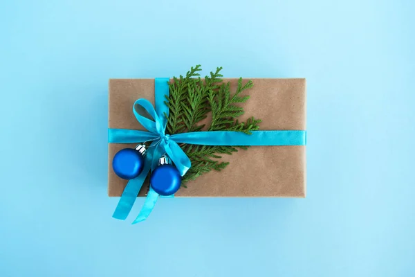 Luxe-geschenketui van Kraft papier, blauw lint gewikkeld en ingericht fir takken en blauwe kerstballen op de blauwe achtergrond, bovenaanzicht. Kerstcadeau. — Stockfoto