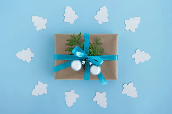 Luxe-geschenketui van Kraft papier, blauw lint gewikkeld en ingerichte fir takken en zilveren kerstballen met Witboek fir tree rond op de blauwe achtergrond, bovenaanzicht. — Stockfoto