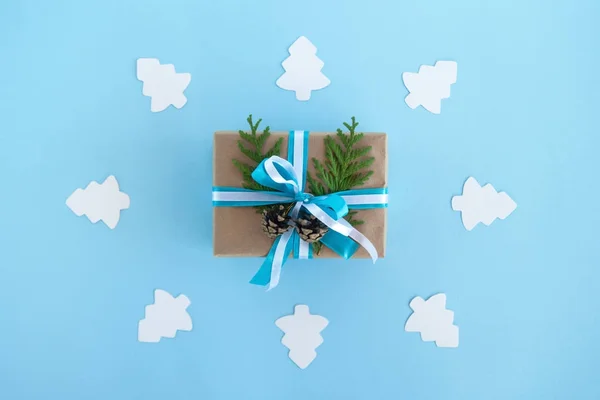 Luxe-geschenketui gewikkeld van Kraft papier, blauwe en witte linten en ingerichte fir takken en pinecones op de blauwe achtergrond met Witboek fir tree, bovenaanzicht. — Stockfoto