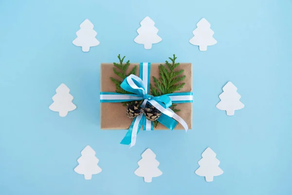 Luxe-geschenketui gewikkeld van Kraft papier, blauwe en witte linten en ingerichte fir takken en pinecones op de blauwe achtergrond met Witboek fir tree, bovenaanzicht. — Stockfoto