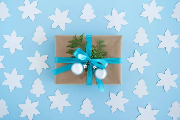 Caixa de presente envolta de papel artesanal, fita azul e ramos de abeto decorados e bolas de Natal de prata no fundo azul com abeto de papel branco e estrela, vista superior . — Fotografia de Stock