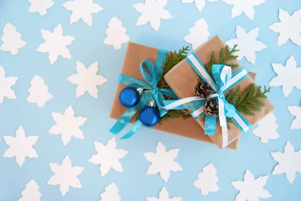 Дві подарункові коробки, обгорнуті ремісничим папером, синьо-білою стрічкою та прикрашені ялинковими гілками, сині різдвяні кульки та піктограми на синьому фоні з білим паперовим ялинкою та зіркою, вид зверху . — стокове фото