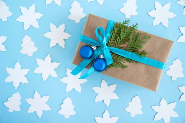 Caixa de presente envolta de papel artesanal, fita azul e ramos de abeto decorados e bolas de Natal azuis no fundo azul com abeto de papel e estrela, vista superior . — Fotografia de Stock