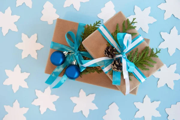 Duas caixas de presente embrulhadas de papel artesanal, fita azul e branca e ramos de abeto decorados, bolas de Natal azuis e pinhas no fundo azul com abeto de papel branco e estrela, vista superior . — Fotografia de Stock