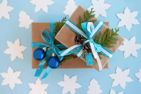 Twee geschenkdozen verpakt van Kraft papier, blauw en wit lint en ingerichte fir takken, blauwe kerstballen en pinecones op de blauwe achtergrond met papier fir tree en de sterren, bovenste weergave. — Stockfoto