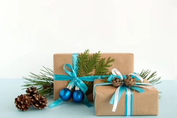 Caixas de presente de Natal embrulhadas de papel artesanal, fitas azuis e brancas, decoradas de ramos de abeto, cones de pinheiro e bolas de Natal no fundo azul e branco . — Fotografia de Stock