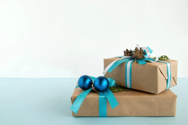 Két karácsonyi díszdobozok csomagolva, kézműves papír, kék és fehér szalagokkal díszített, a fenyő ágak, fenyő kúpok, és karácsonyi golyókat a kék és a fehér háttér. — Stock Fotó