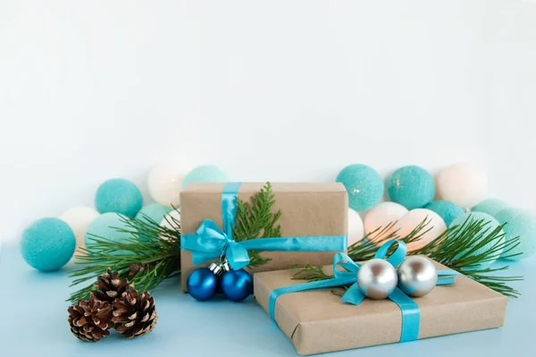 Duas caixas de presente de Natal embrulhadas de papel artesanal, fitas azuis e brancas, decoradas de ramos de abeto, bolas de Natal e cones de pinho no fundo azul e branco com luzes de Natal . — Fotografia de Stock