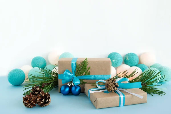 Duas caixas de presente de Natal embrulhadas de papel artesanal, fitas azuis e brancas, decoradas de ramos de abeto, cones de pinho e bolas de Natal no fundo azul e branco com luzes de Natal . — Fotografia de Stock