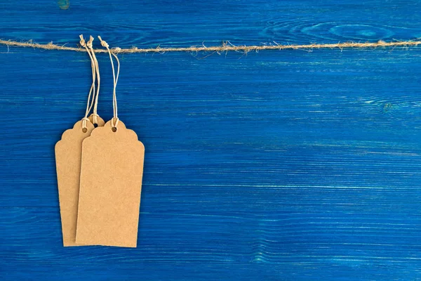 Tres etiquetas o etiquetas de precio de papel en blanco marrón colgadas de una cuerda en el fondo azul de madera. — Foto de Stock