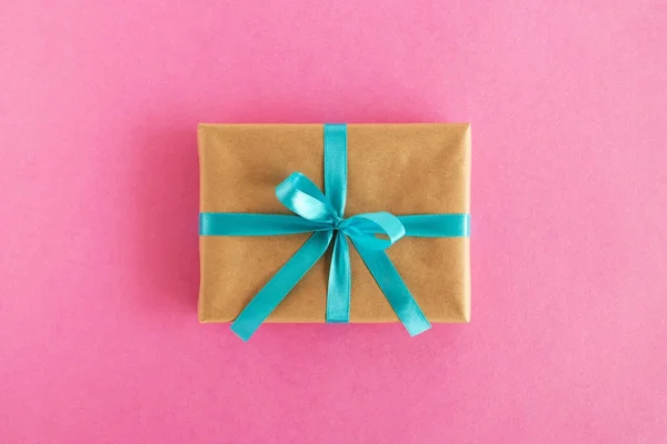 Geschenkverpackung aus Bastelpapier und blauem Band auf rosa Hintergrund, Ansicht von oben. — Stockfoto