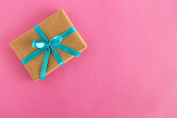 Geschenkverpackung aus Bastelpapier und blauem Band auf rosa Hintergrund, Ansicht von oben. — Stockfoto