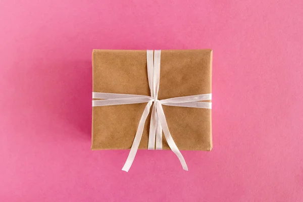 Geschenkverpackung aus Bastelpapier und weißem Band auf rosa Hintergrund, Ansicht von oben. — Stockfoto