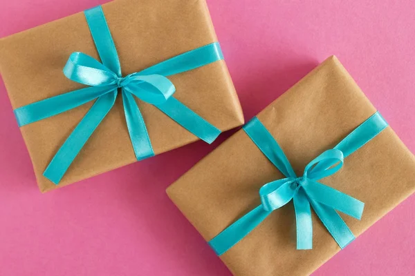 Zwei Geschenkverpackungen aus Bastelpapier und blauem Band auf rosa Hintergrund, Ansicht von oben. — Stockfoto