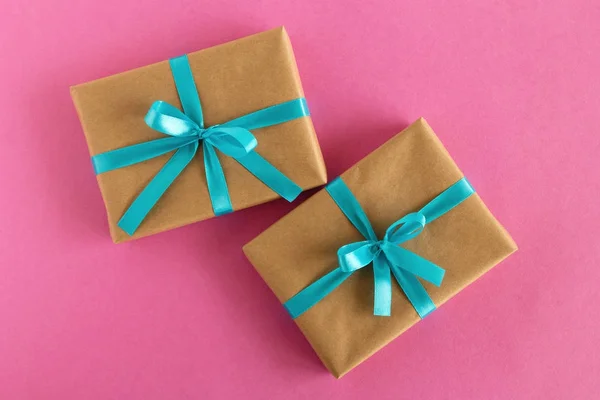 Дві подарункові коробки, обгорнуті ремісничим папером і синьою стрічкою на рожевому фоні, вид зверху . — стокове фото
