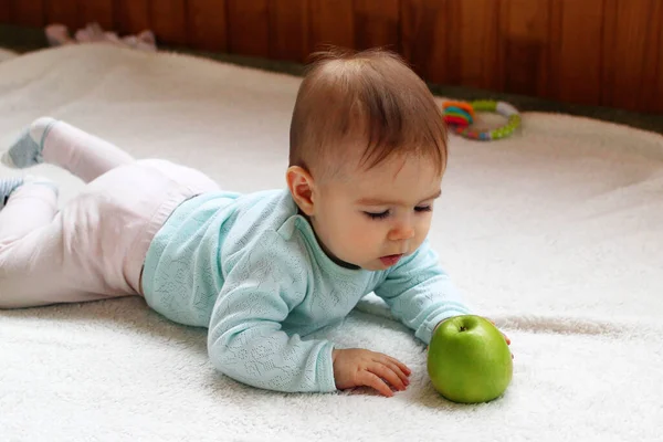 小さな女の子はリビングで白い遊びに横たわっていると緑のリンゴと遊ぶ — ストック写真