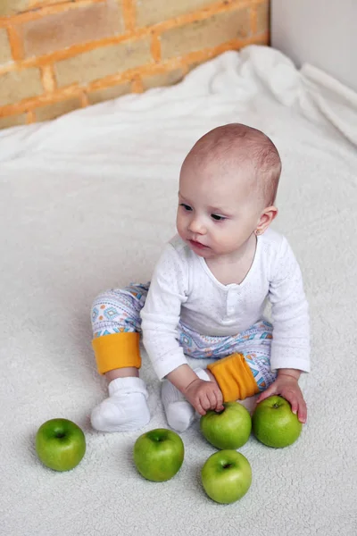 1歳の少女は 緑のリンゴで遊ぶ白い部屋に座っています 子供の健康食品 — ストック写真