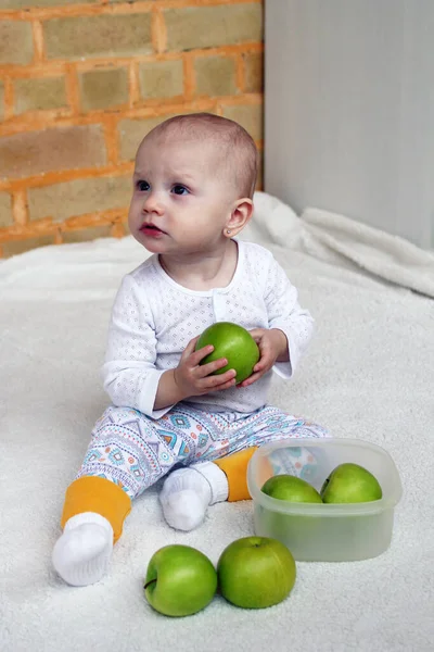 小さな女の子はプラスチック製の容器に緑のりんごで遊ぶ白い部屋に座っています — ストック写真