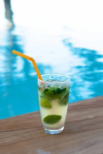 Glass of iced mojito cocktail at the edge of swimming pool. Outdoor pool background with copy space.