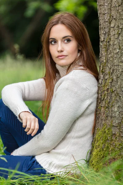 Schöne junge Frau sitzt an Baum gelehnt — Stockfoto