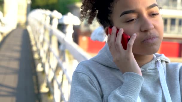 4K clipe de vídeo de bela raça mista afro-americana menina adolescente mulher em uma ponte sobre um rio, falando em um telefone celular — Vídeo de Stock